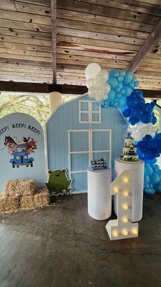 blue and white balloons are hanging from the ceiling in front of a barn with hay bales