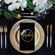 a black and gold place setting with white orchids in the center, along with personalized napkins