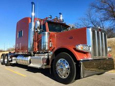 a red semi truck driving down a road next to a field with grass and trees