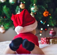 a baby wearing a santa hat laying on top of a bed next to a christmas tree