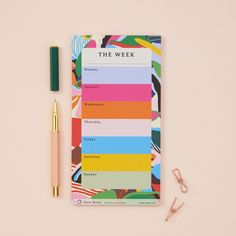 the weekly planner next to a pen and eyeglasses on top of a pink surface