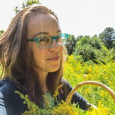 a woman with glasses holding a basket in the middle of a field full of yellow flowers