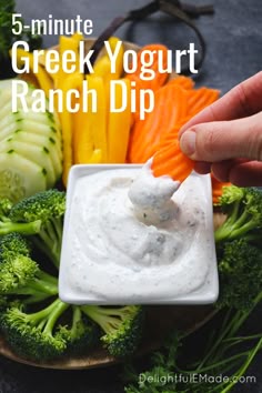 a hand dipping ranch dip into broccoli and carrots