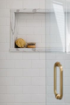 a white tiled bathroom with a gold handle on the shower door and a yellow brush