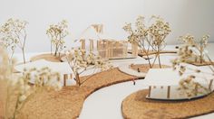 a model of a house surrounded by small trees and bushes with white flowers on the ground