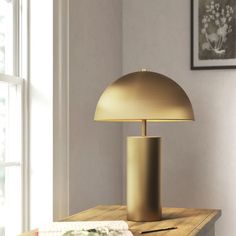 a table lamp sitting on top of a wooden table next to a window with pictures hanging above it