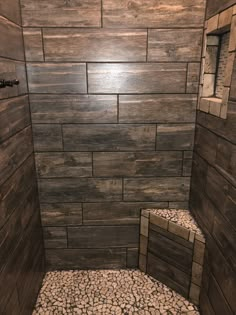 a walk in shower sitting next to a wooden wall and floor covered in pebbles on the ground