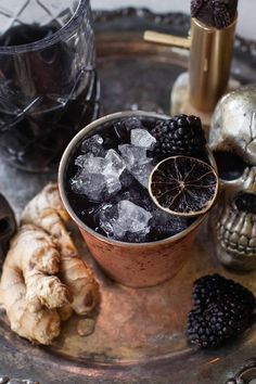 a drink in a copper cup with ice and blackberries on the rim next to skulls