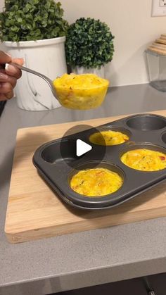 a person is holding a spoon over some food in a muffin tin on a counter