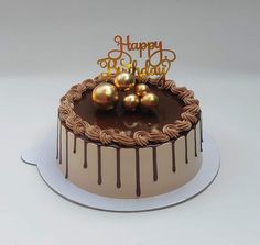 a birthday cake with chocolate icing and three golden balls on top that says happy birthday