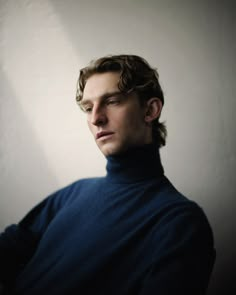 a man in a blue turtle neck sweater looking off into the distance with his hands on his hips