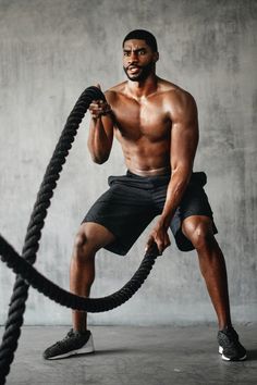 a shirtless man holding a rope while standing in front of a wall