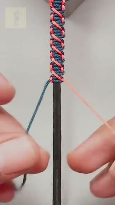 two hands are working on the end of a piece of string with red and blue thread