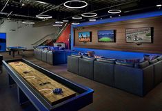 a bowling table in the middle of a room with couches, tables and televisions