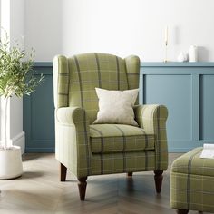 a green chair and ottoman in a room with blue paneled walls, wood flooring and a potted plant