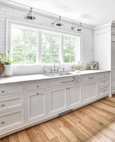 a kitchen with white cabinets and wood flooring is pictured in this image, there are three lights on the windows above the sink