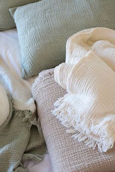 a blanket and pillows on top of a bed with white linens in the background