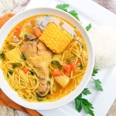 a white bowl filled with chicken noodle soup next to rice and carrots on a plate