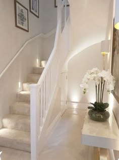 there is a vase with white flowers on the table next to the stairs in this house