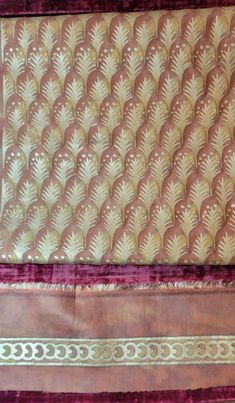 an old piece of cloth with gold and red designs on it's edges, sitting on a purple surface