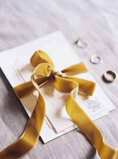 a close up of a ribbon on a piece of paper with two wedding rings in the background