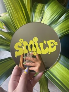 someone holding up a sticker with the word smile written on it in front of a green plant