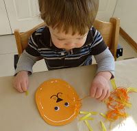 a young boy sitting at a table with an orange paper plate and scissors in front of him