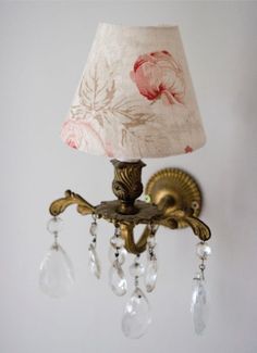 a wall light with a fabric shade on it and crystal beads hanging from the arm