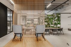 two chairs in front of a wooden screen with plants on the wall and tables behind them