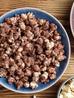 a blue bowl filled with chocolate covered popcorn next to two bowls full of cereal on a wooden table