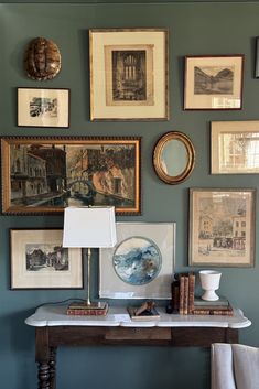 a wall with many pictures on it and a lamp next to the table in front