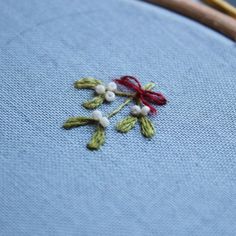 a close up of a cross stitch on a piece of blue fabric with red and white beads