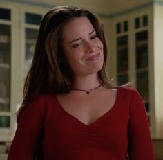 a woman in a red shirt is smiling and looking at the camera while wearing a necklace