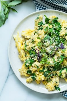 scrambled eggs with spinach and onions on a white plate next to a blue towel