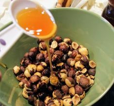 someone pouring honey into a bowl filled with nuts