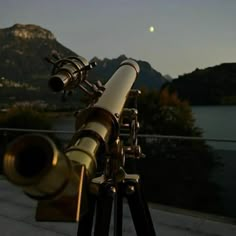 a telescope on a tripod with the moon in the sky behind it and mountains in the background