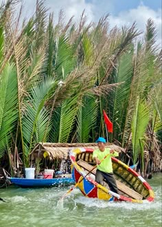 a man riding on the back of a colorful boat down a river next to palm trees