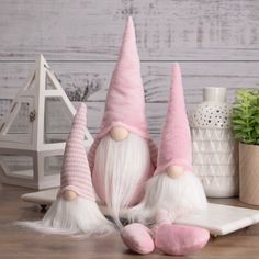 two pink and white gnomes sitting on top of a table next to a potted plant