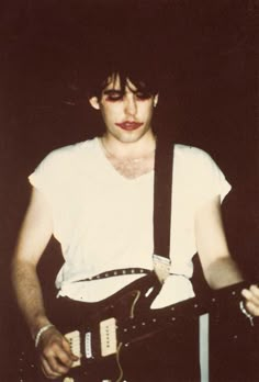 a young man holding an electric guitar in his right hand and looking at the camera