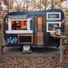 a blue and white trailer parked in the woods with lights on it's windows