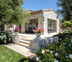 a stone house with pink flowers in the front and stairs leading up to it's entrance