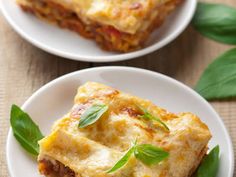 a white plate topped with lasagna on top of a table next to tomatoes