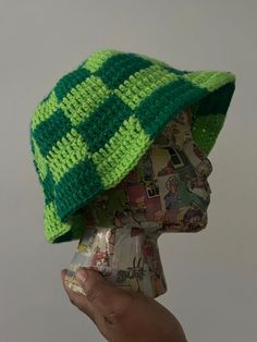 a hand holding up a knitted green and yellow hat on top of a mannequin's head