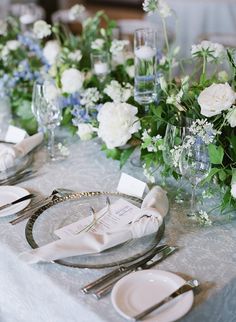 the table is set with white and blue flowers, silverware, and napkins