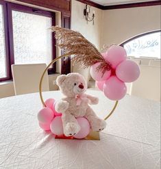 a teddy bear sitting on top of a table next to some pink balloons and grass