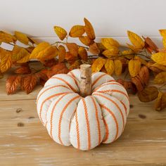 an orange and white striped pumpkin sitting on top of a wooden table next to leaves