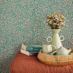 a vase with flowers and two mugs on a table in front of a wallpaper