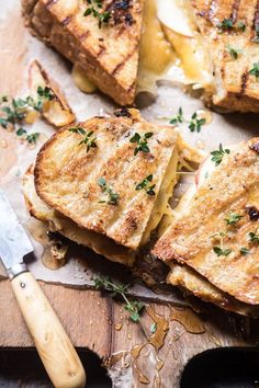 grilled cheese sandwiches with fresh herbs on a wooden cutting board next to a knife