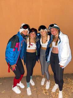 four girls are posing for the camera in front of a wall wearing snow gear and ski goggles