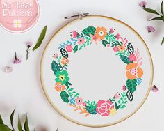 a cross stitch wreath with flowers and leaves on it, next to the embroidery pattern